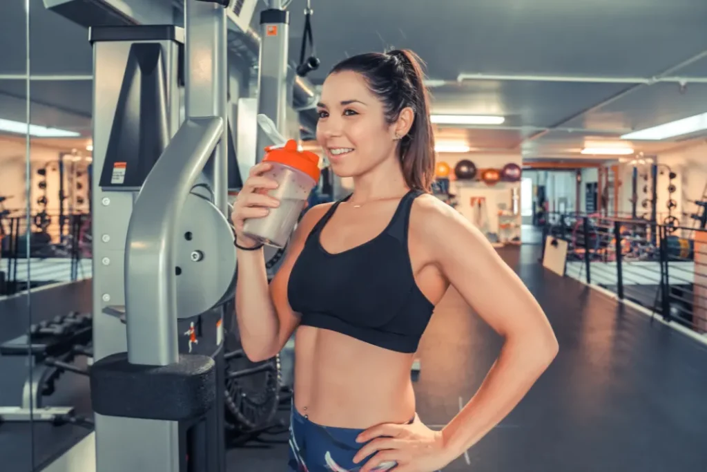 Lean Woman in the gym while drinks protein energy drink.